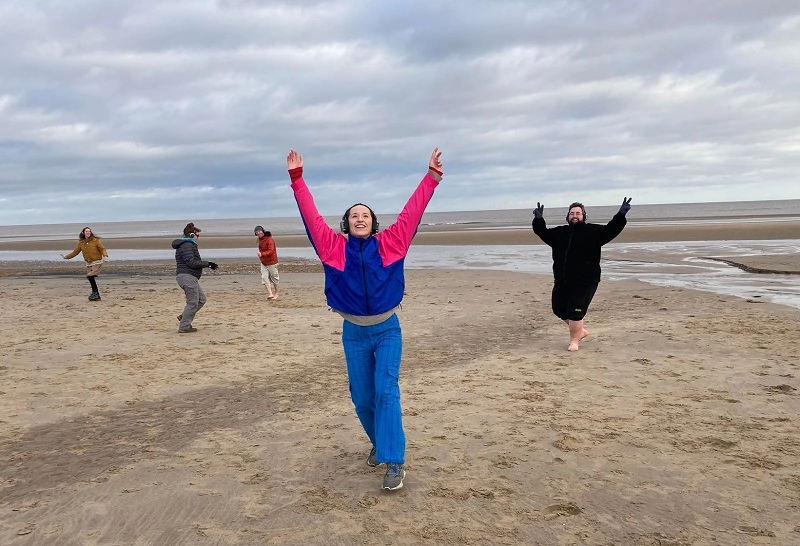 people dancing on a beach with their arms lifted.
