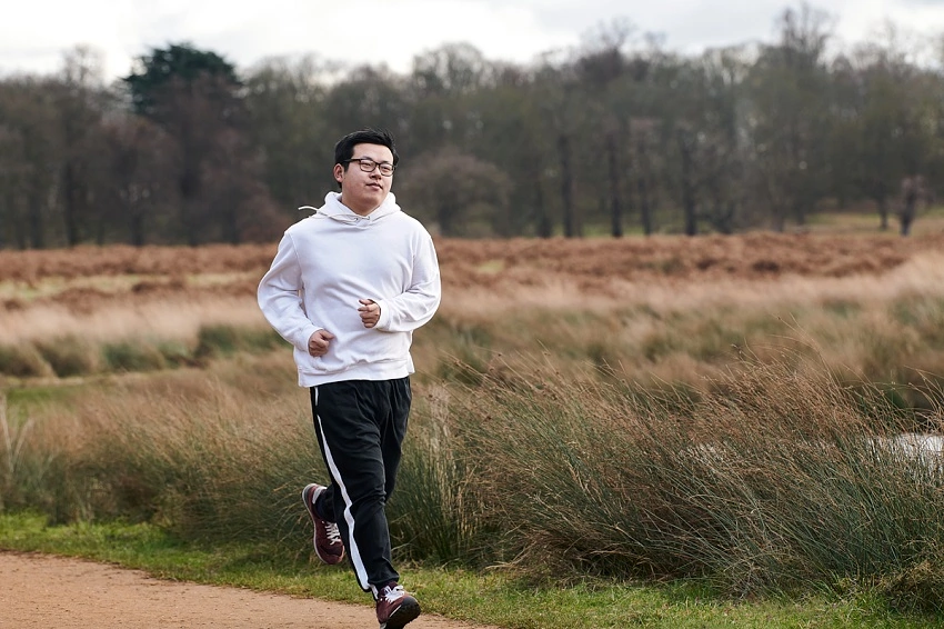 Man in white sweatshirt and black jogging bottoms running on a path next to long grass.