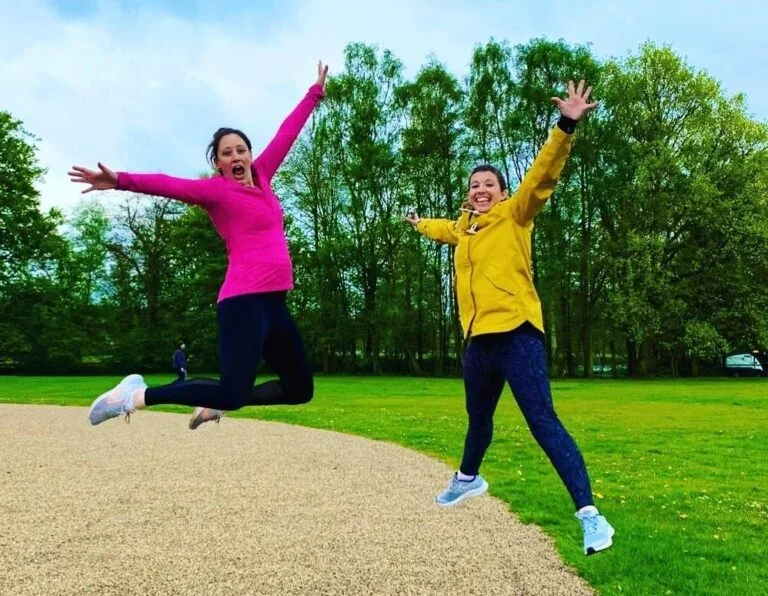 Two women in a park, leaping into the air.