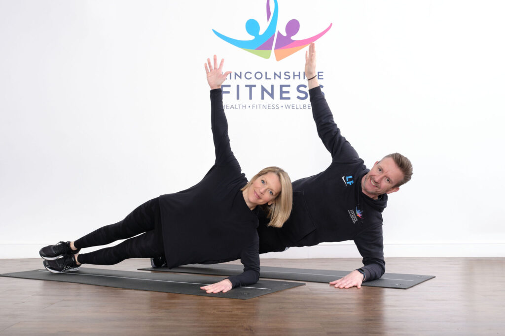a female and male fitness instructor doing sideways plank on floor in front of Lincolnshire Fitness sign on wall