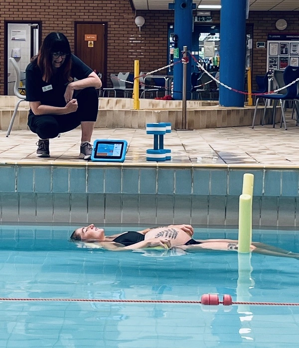 A pregnant woman floating on her back in swimming pool, with instructor at side.
