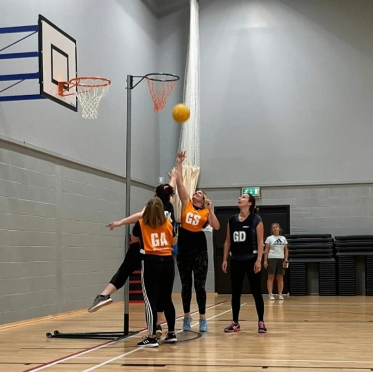 A group of women playing netball, with one throwing the ball into the net.