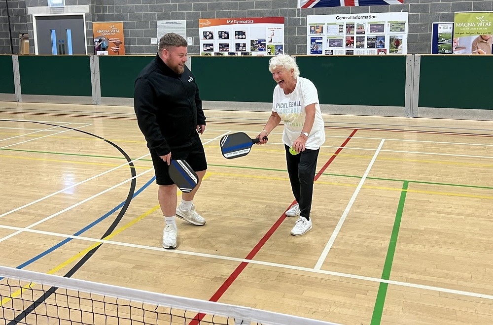 A man coaching a lady with a pickleball paddle.