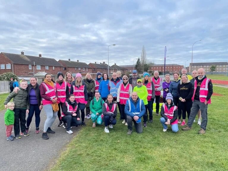 A group of parkrun volunteers, some in pink parkrun hi vis vest, pose for a photo at Yarborough parkrun .