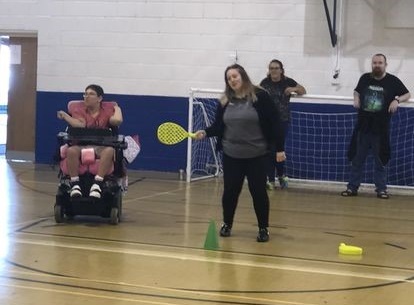 a person in a powerchair and a non disabled person playing with softball bats