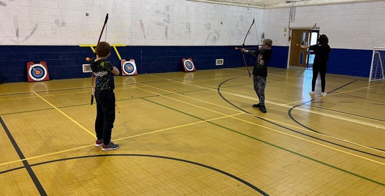 a small group of children taking part in archery in a sports hall.