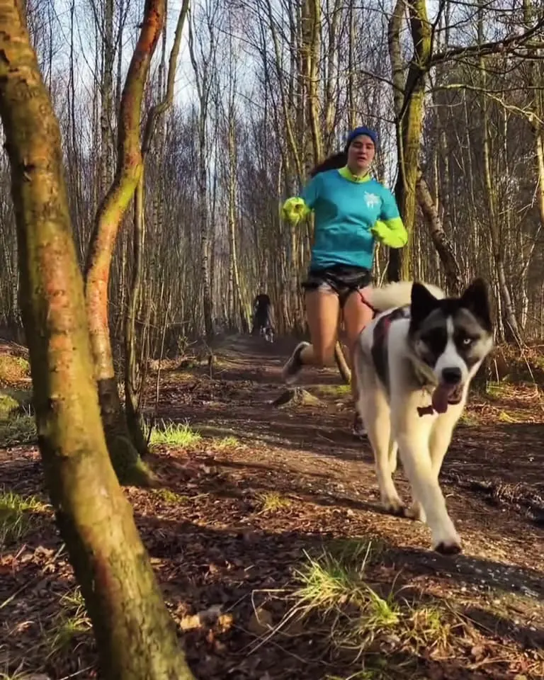 female running on a muddy woodland trail with her dog