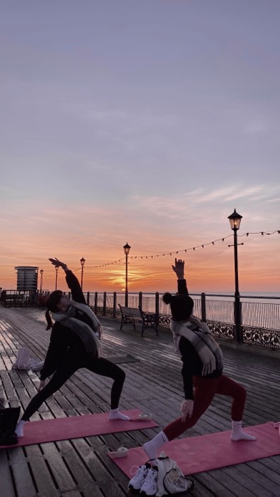 two people doing yoga at sunset on a pier with the sea in the background