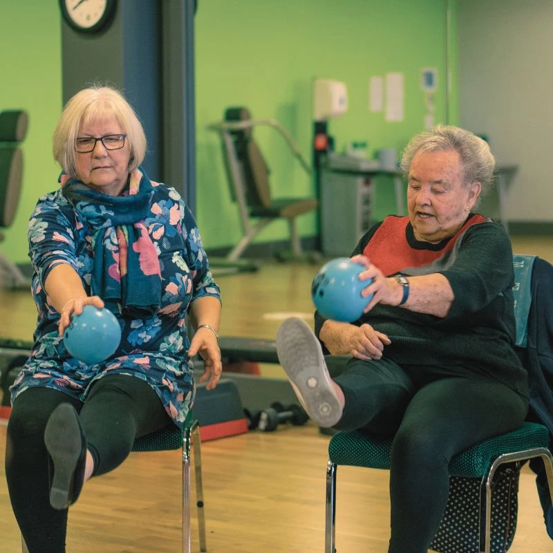 Benefits of Physical Activity - Two older adults doing chair based exercises with a medicine ball in Lincolnshire.