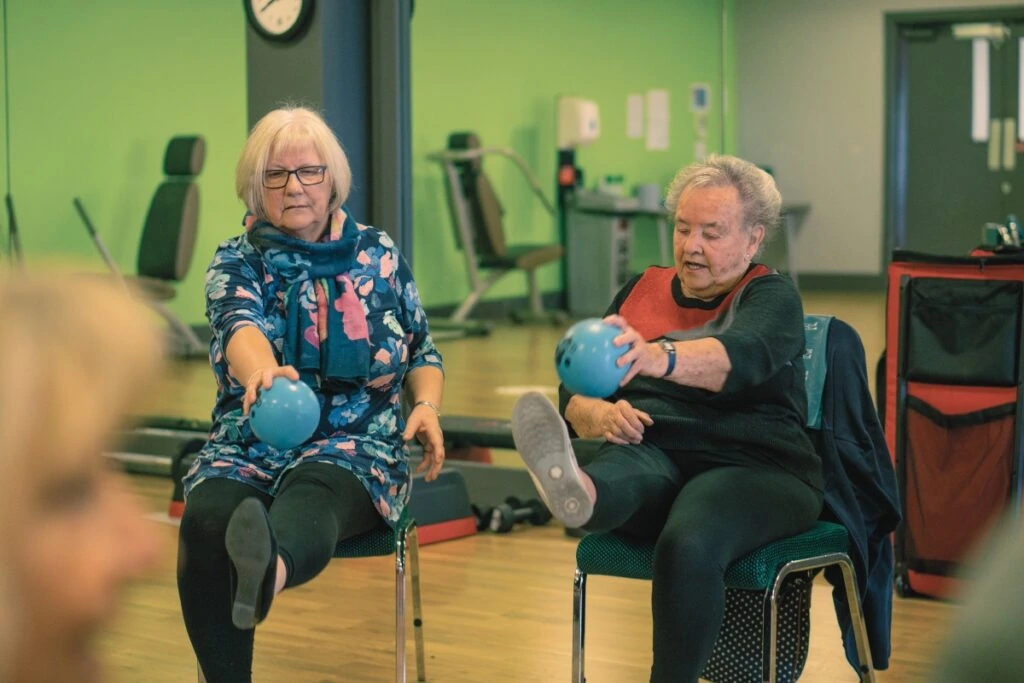 Benefits of Physical Activity - Two older adults doing seated chair based exercises with a medicine ball in Lincolnshire.