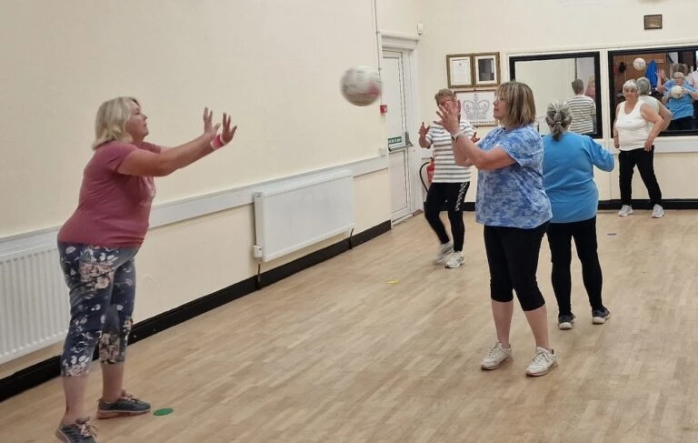 A woman throws a netball to another women in an indoor hall.