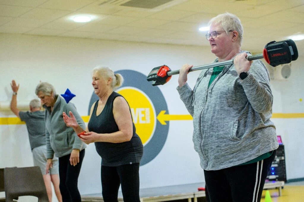 Group exercise class with woman lifting small weighted bar.
