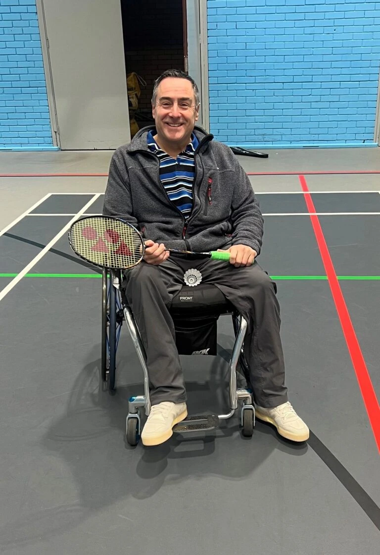 A man in a wheelchair poses for photo holding a badminton racquet.