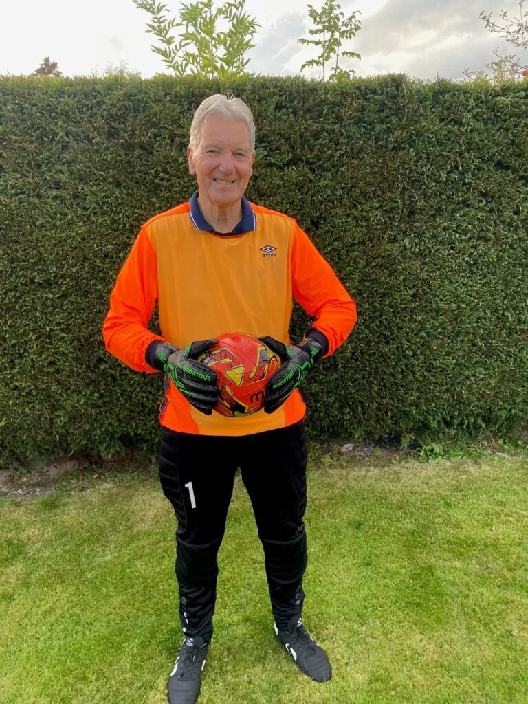 A man wearing orange goalie kit poses for a photo holding a ball.