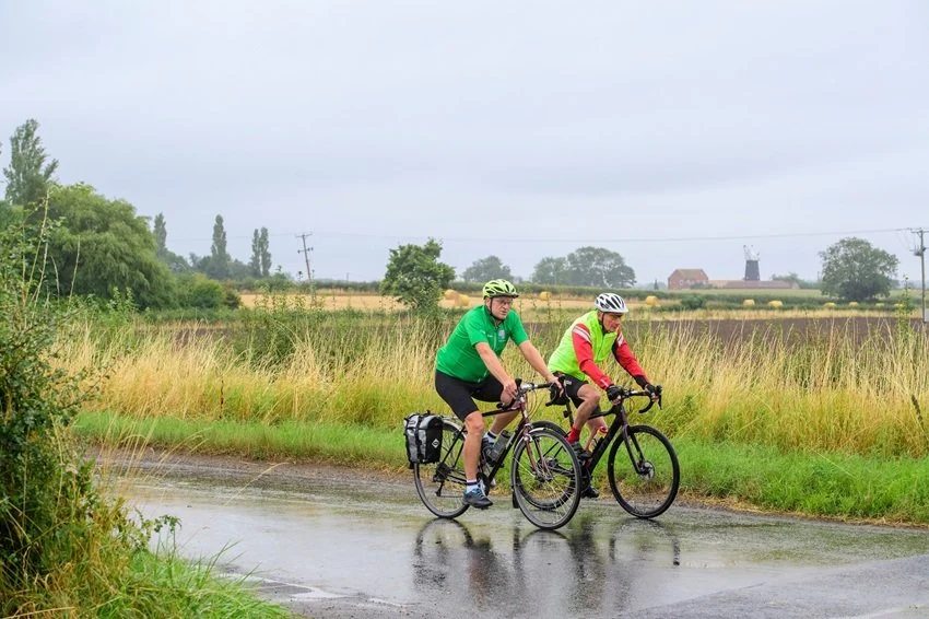 Two men cycling through the wet countryside